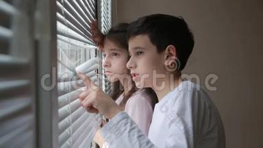 小女孩和男孩，兄妹，双胞胎从窗户透过百叶窗看着街道